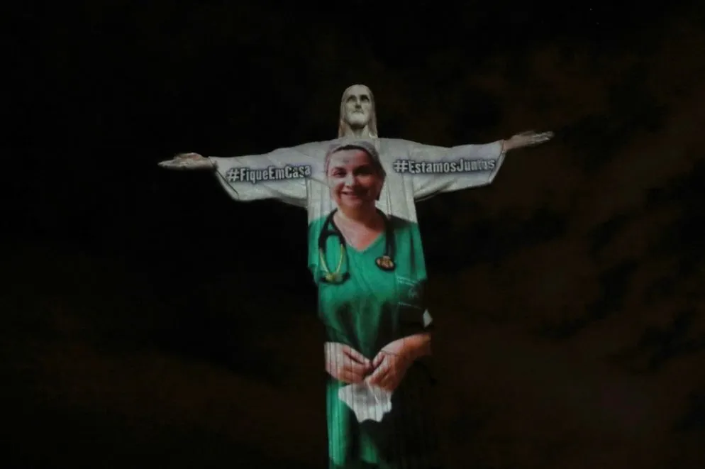 Tra le grandi braccia aperte del Cristo Redentore viene proiettata l'immagine di un'infermiera