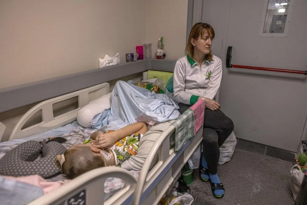 Una madre siede accanto al figlio ricoverato, e che nei giorni scorsi è stato spostato nel seminterrato