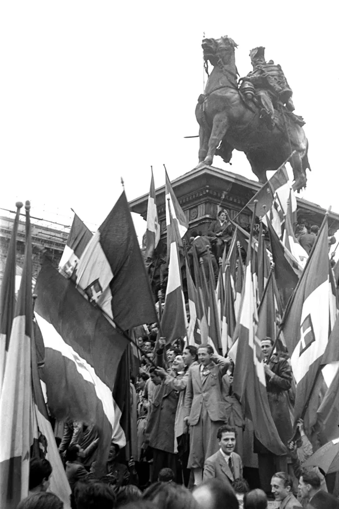 Federico Patellani, Dopo la manifestazione monarchica in piazza del Cannone, manifestanti sventolano la bandiera del Regno d'Italia sotto la statua di Vittorio Emanuele II in piazza del Duomo. Milano, 26 maggio 1946 © Archivio Federico Patellani, courtesy Regione Lombardia / Museo Nazionale di Fotografia, Milano-Cinisello Balsamo