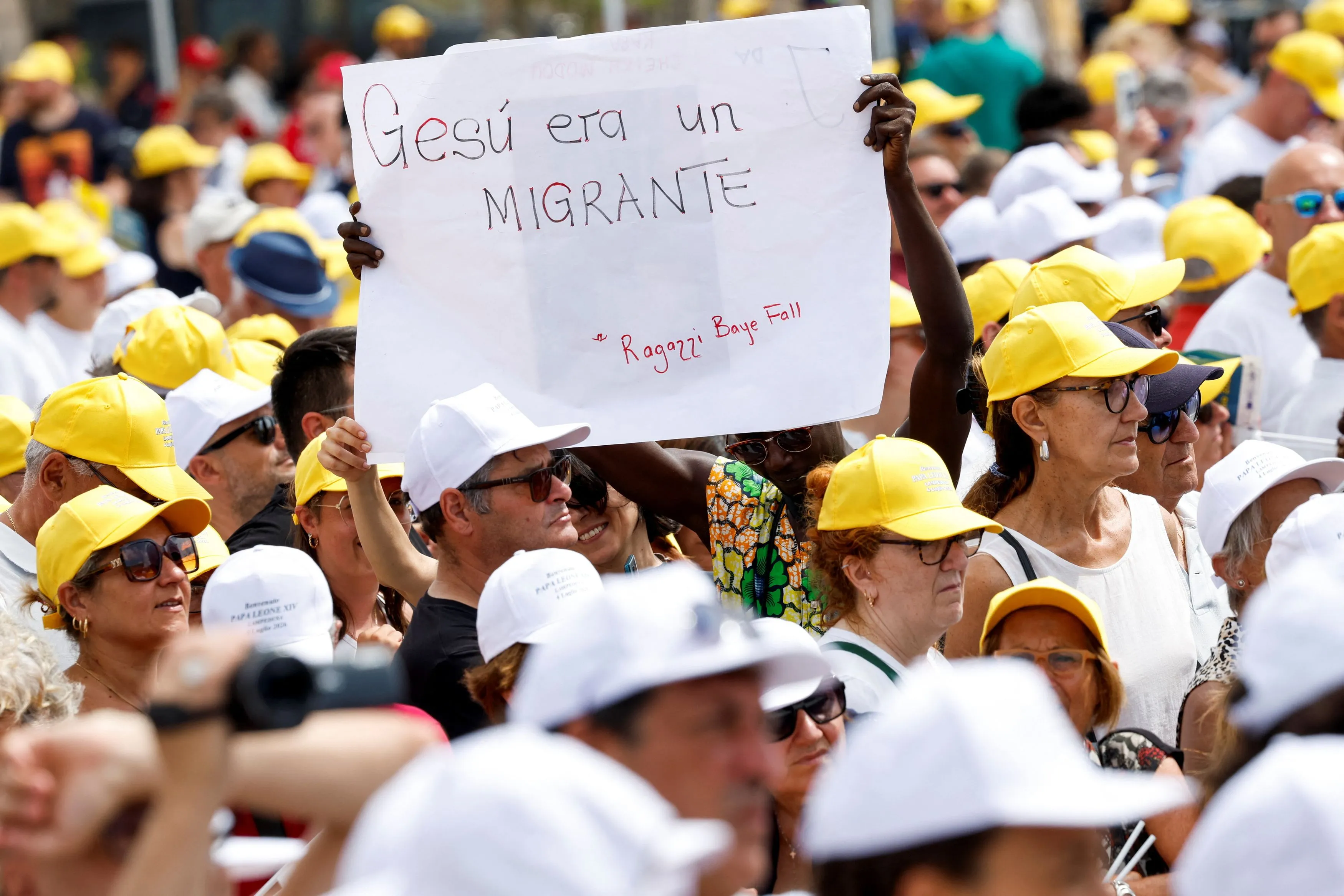 Il popolo dei fedeli che partecipa alla Santa Messa celebrata dal Papa a Lampedusa. Su un cartello il messaggio: "Gesù era un migrante" / Reuters_Remo Casilli