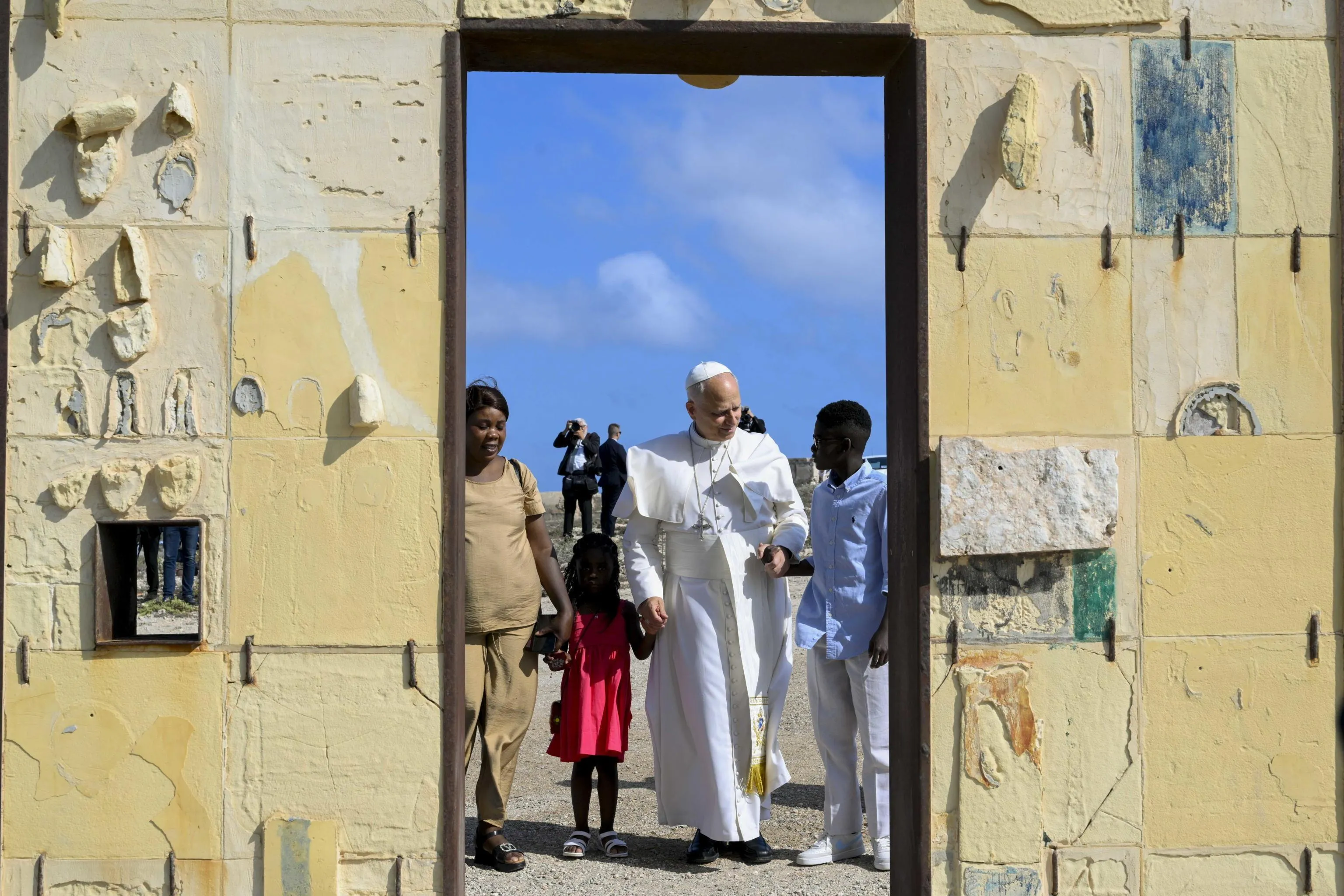 La visita di Papa Leone XIV a Lampedusa, il 4 luglio 2026. Prevost alla Porta d’Europa, il monumento che rende omaggio ai migranti ed è simbolo della frontiera più a sud dell’Italia e del continente; è accompagnato da una famiglia di migranti con i bambini / Epa - Vatican Media