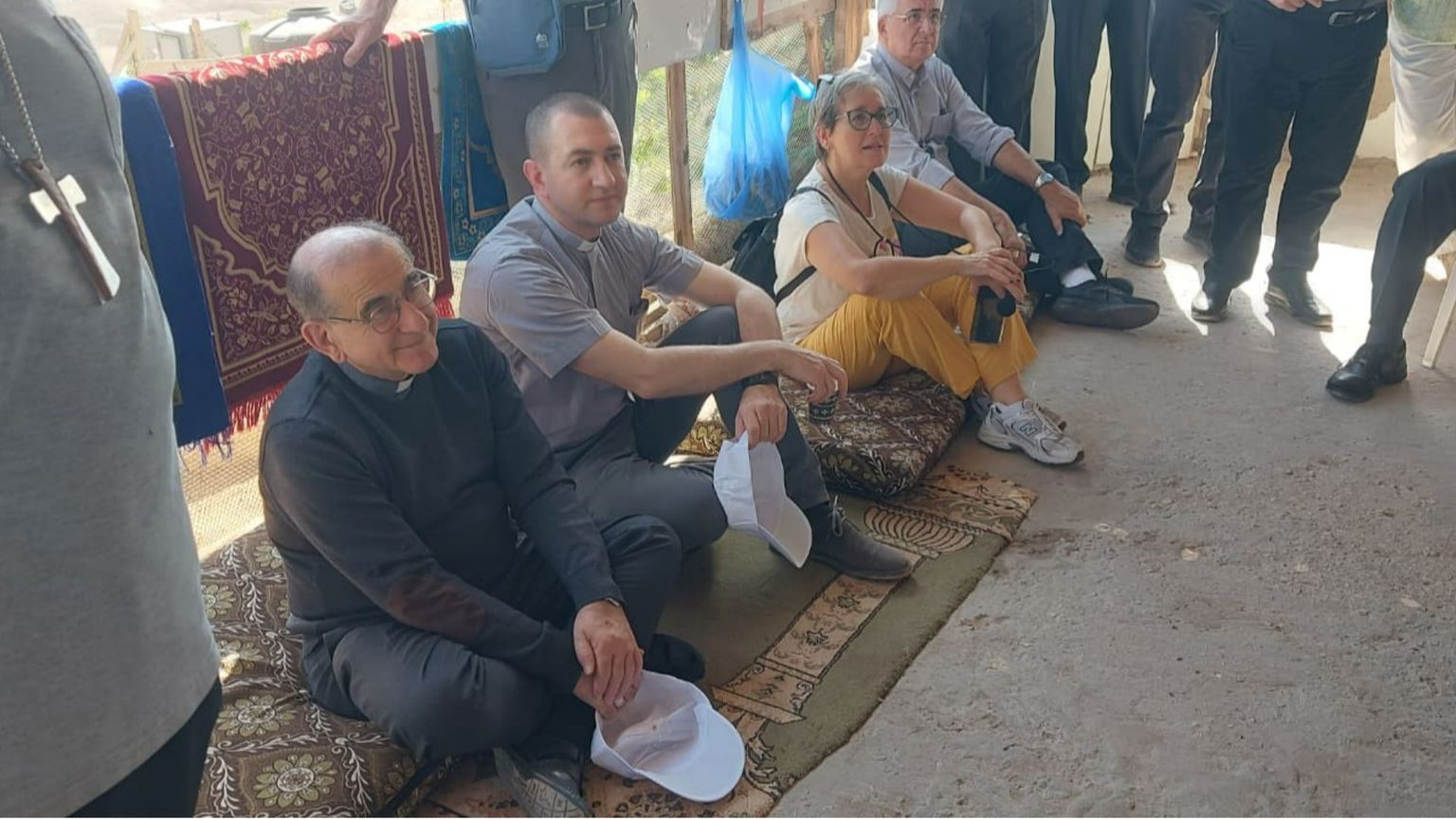 Nella fotto si vedono l’arcivescovo di Milano Mario Delpini seduto a terra in un villaggio beduino con altri partecipanti al recente pellegrinaggio in Terra Santa