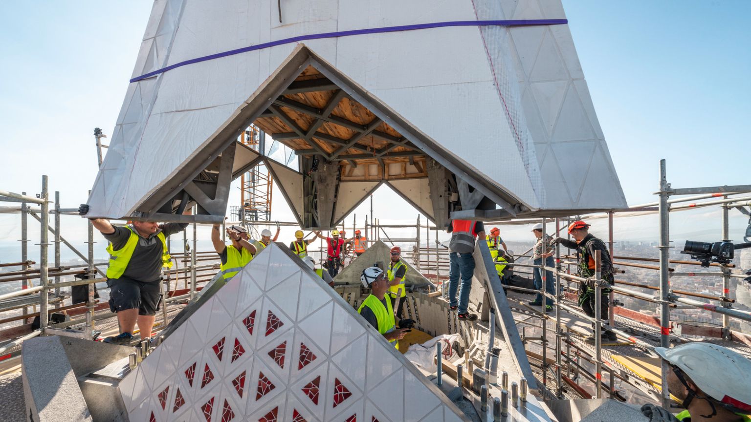 Il braccio inferiore della croce collocato sulla Torre di Gesù Cristo con operai a lavoro