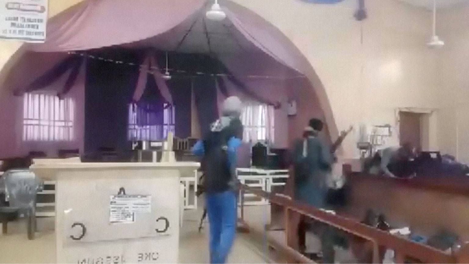 In un fermo immagine da video, due uomini armati, in piedi di spalle, a fianco di un altare e tra le panche
