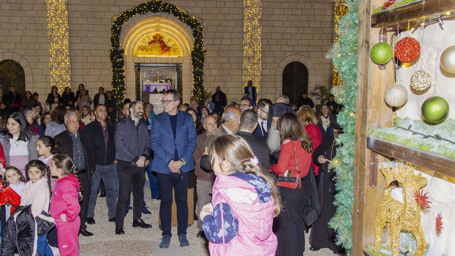 Bambini e adulti chiacchierano e sorridono in una piazzetta davanti alla chiesa addobbata con luci e decorazioni natalizie