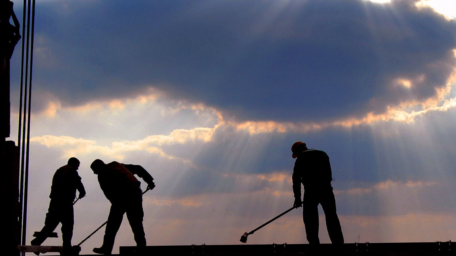 L'immagine mostra tre uomini che stanno lavorando su un ponteggio alla luce di un tramonto