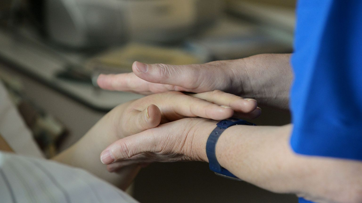 Un'infermiera stringe le mani di un malato di cancro in un reparto di cure palliative