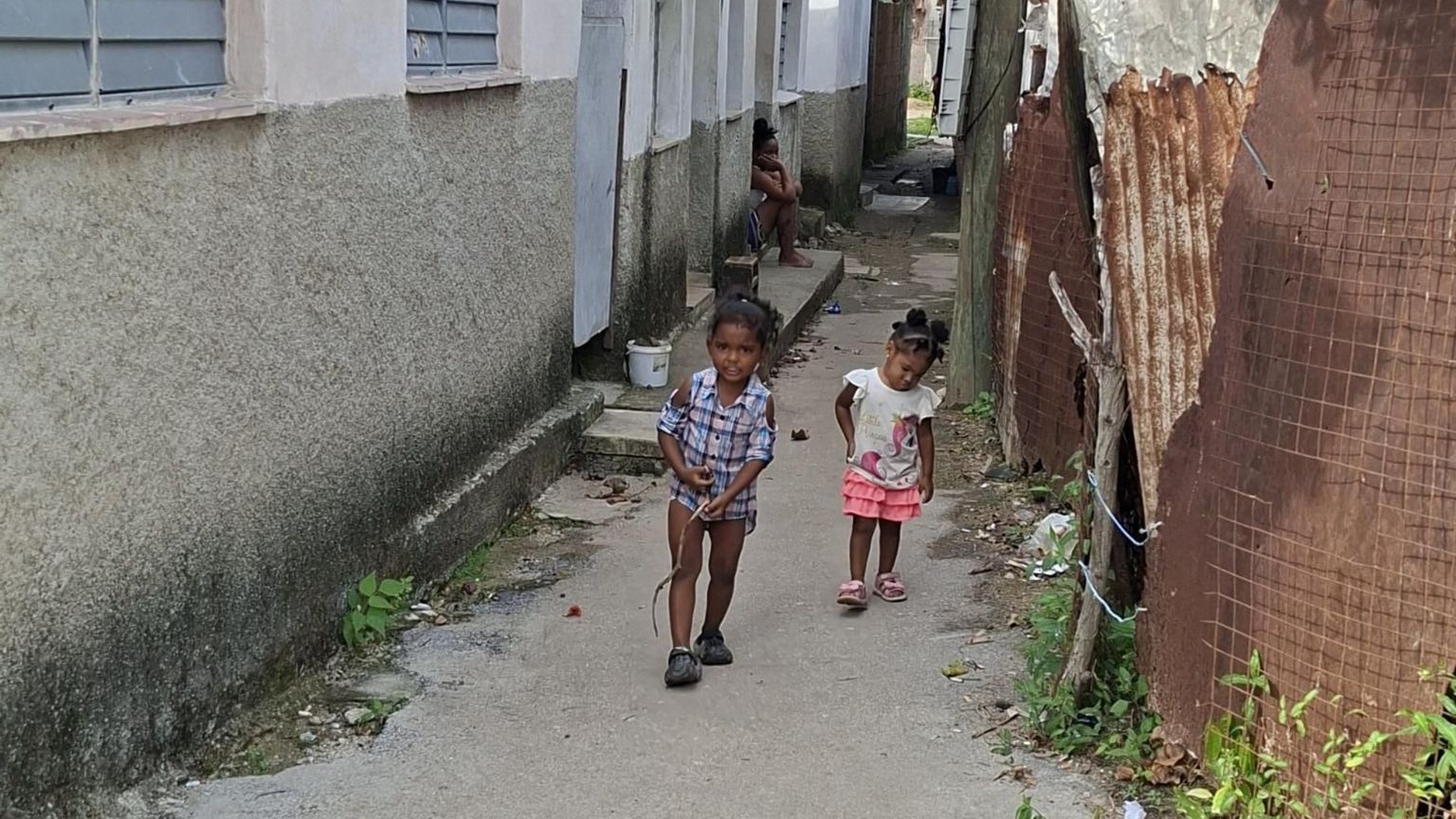Due bambini cammino in un viottolo sterrato di una baraccopoli dell'Avana su cui si affacciano casupole di compensato e lamiera