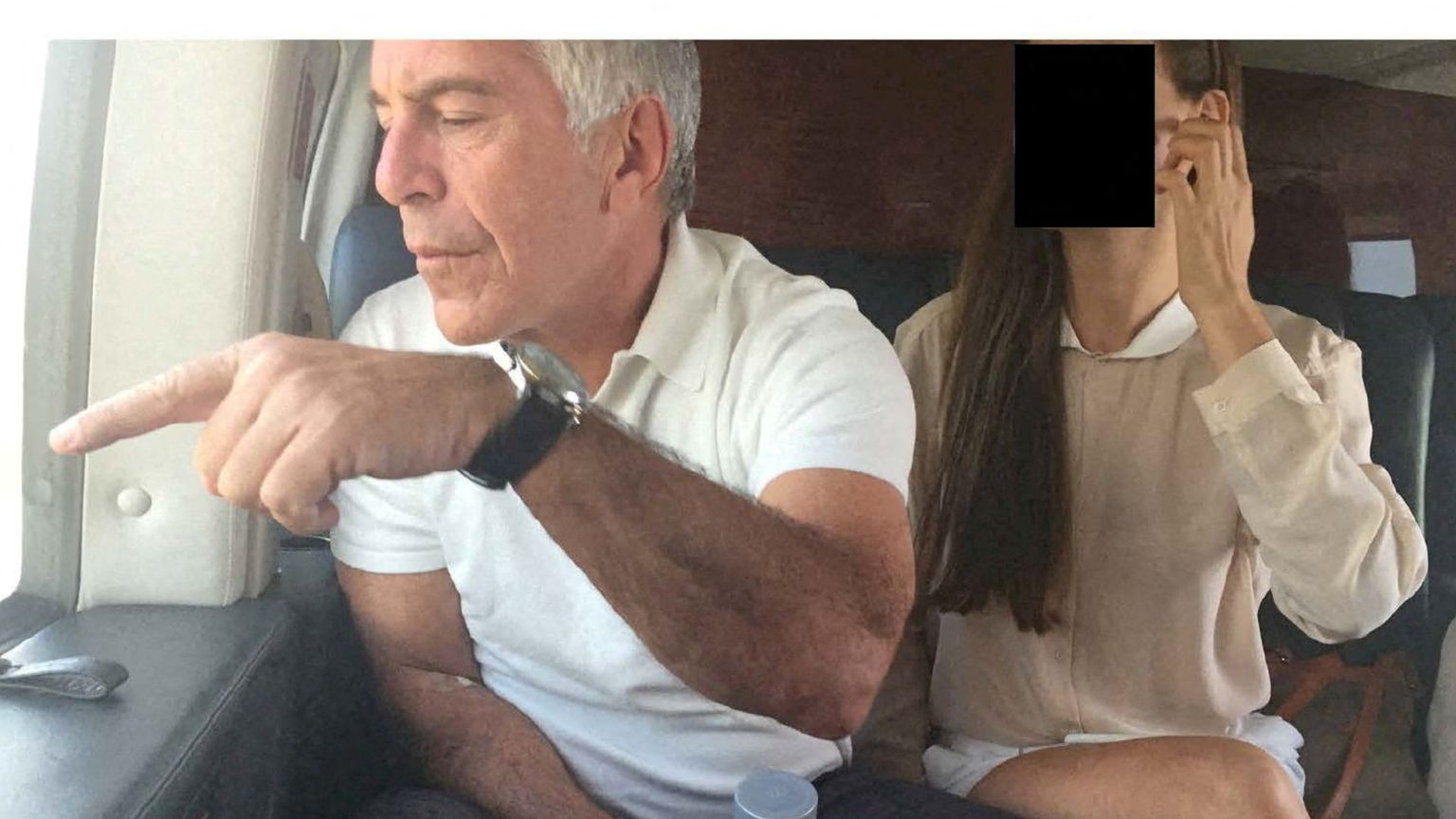 Il finanziere Jeffrey Epstein a bordo di un aereo indica qualcosa dal finestro. Al suo financo una donna il cui volto è stato oscurato per ragioni di riservatezza