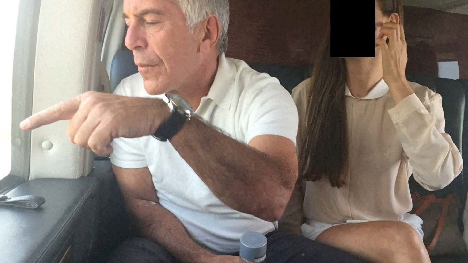 Il finanziere Jeffrey Epstein a bordo di un aereo indica qualcosa dal finestro. Al suo financo una donna il cui volto è stato oscurato per ragioni di riservatezza