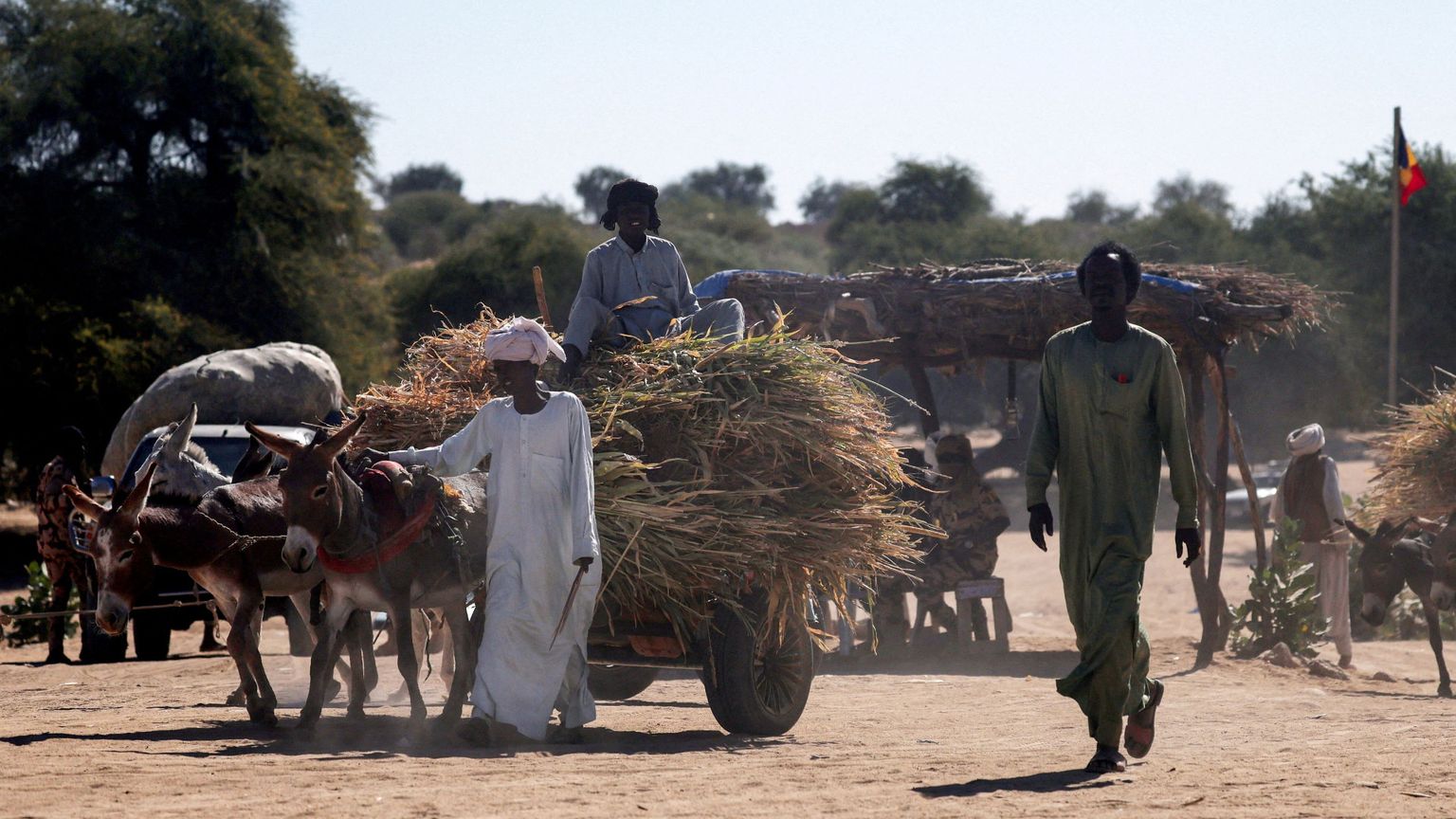 Una donna africana vestita di bianco guida a piedi un carretto trainato da un asino con a bordo il figlio e i pochi averi: fugge dalla guerra in Sudan