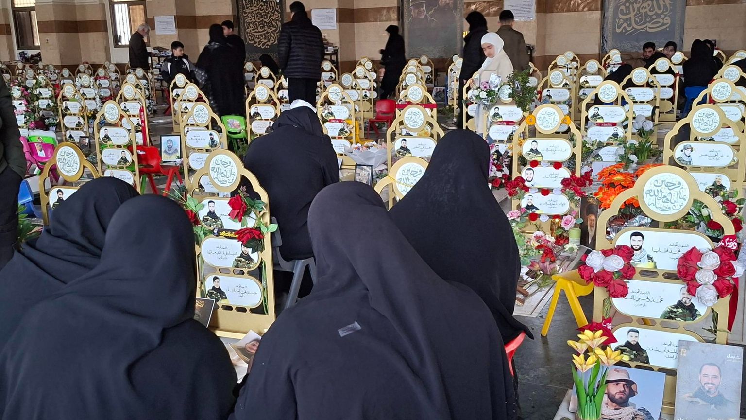 Donne velate di nero, di spalle davanti alle tombe ornate di nastri gialli e fiori con le fotografie di giovanissimi