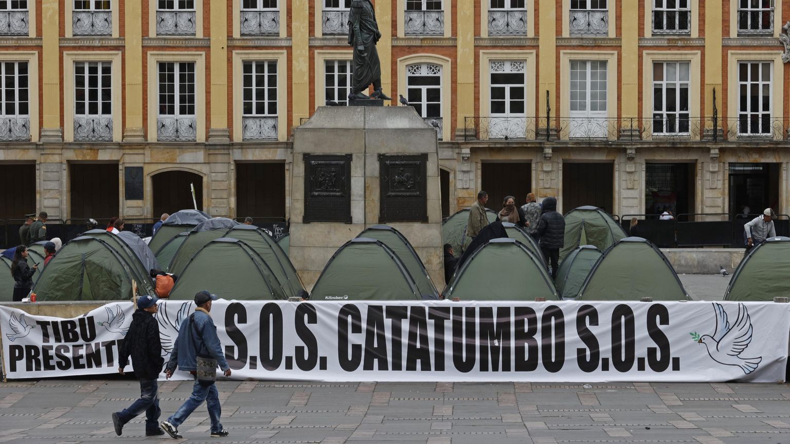 Due persone passano davanti a una serie di tende nella piazza Bolívar di Bogotà e alla scritta: "S.O.S. Catatumbo". Con l'iniziativa, i promotori hanno voluto denunciare la violenza nella regione ocolombiana