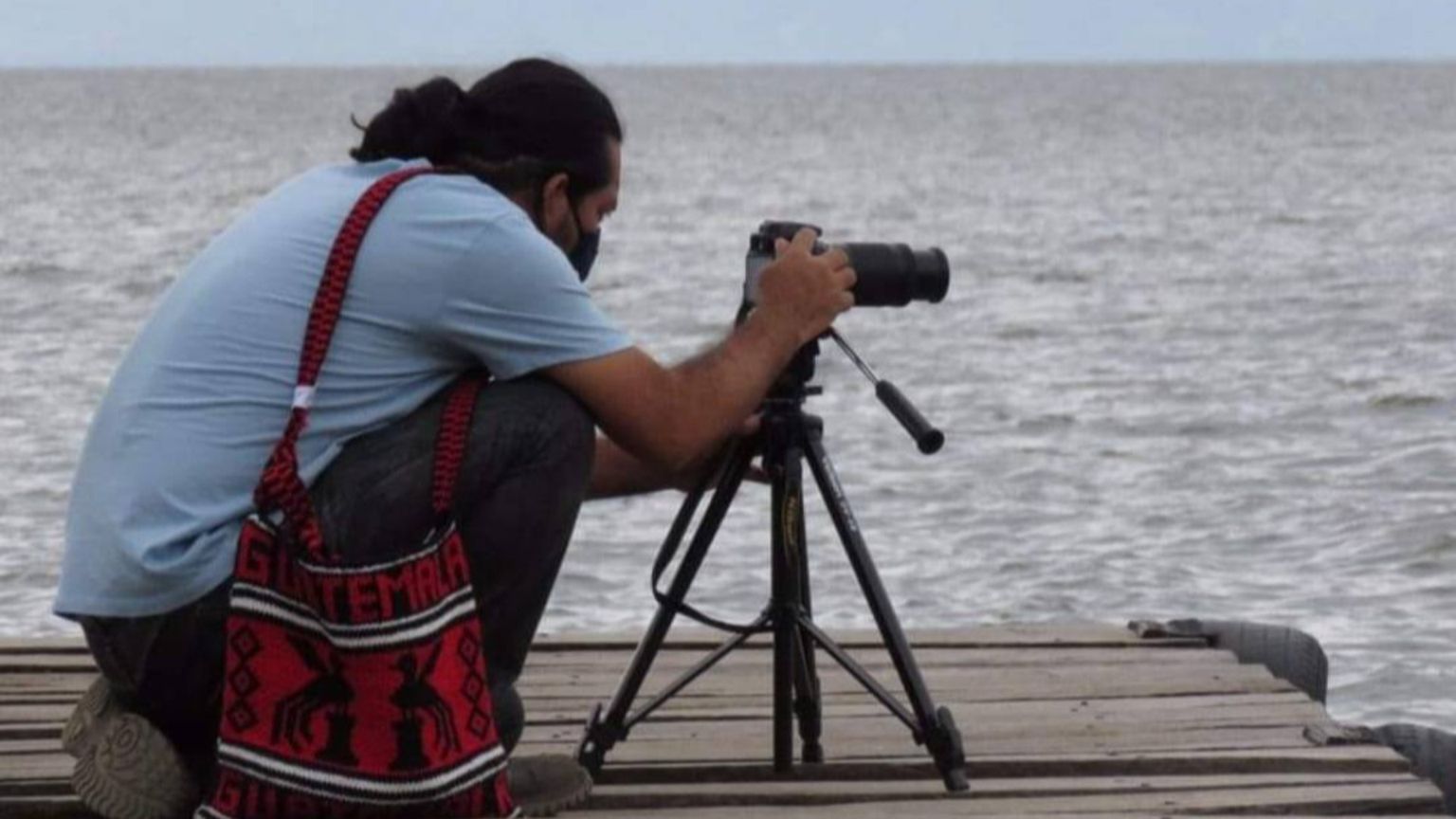 Carlos Choc è inginocchiato sulle sponde di un lago per scattare una fotografia con la sua macchina