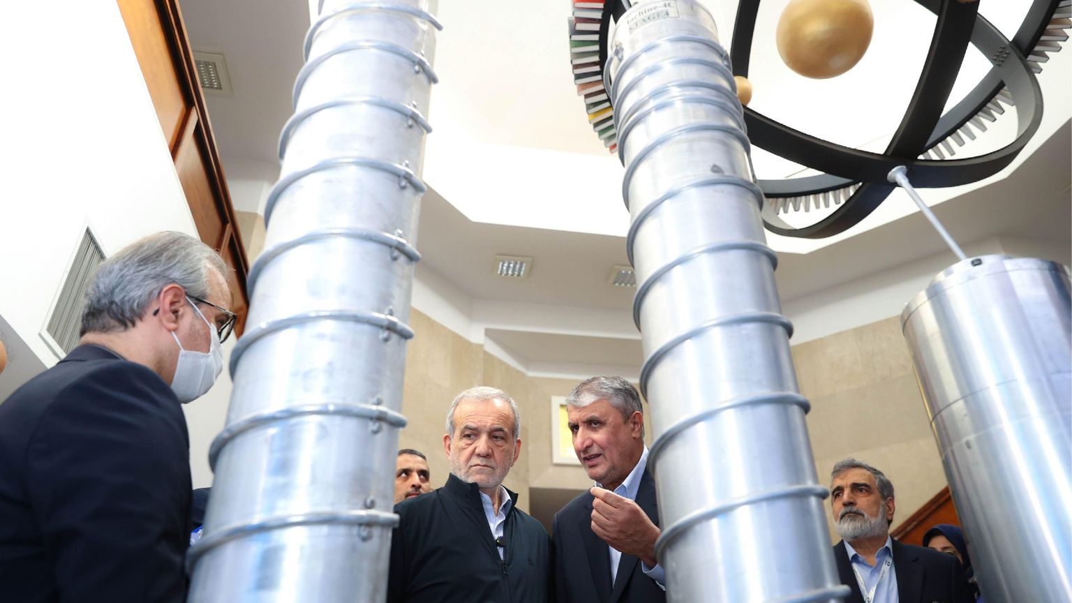 Un gruppo di funzionari iraniani e il presidente Massud Pezeshkian ispezionano dei grandi cilindri grigi in uno degli impianti del programma nucleare