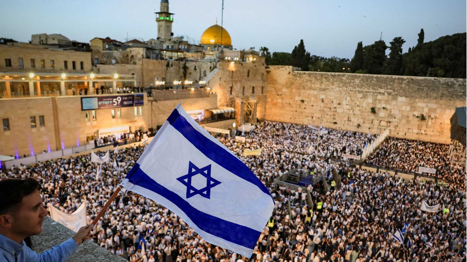 Un giovane nazionalista agita una bandiera israeliana da un balcone davanti alla folla radunata al Muro Occidentale di Gerusalemme