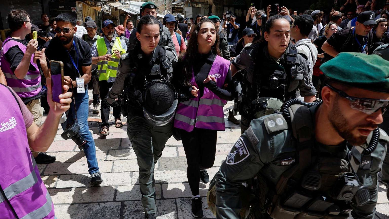 Una ragazza con un giubbino catarifrangente rosa, indossato dagli attivisti di "Standing Together", portata via da due poliziotte in mezzo a una manifestazione