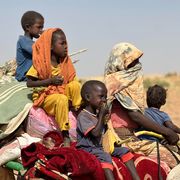 Una donna con la testa coperta e quattro bambini, tutti seduti su un mucchio di sacchi e coperte, a bordo di un carretto trainato da un asino