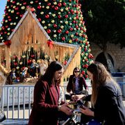 Donne fanno acquisti davanti a una gigantesca stella e a un albero di Natale, sullo sfondo il muro della Basilica della Natività