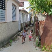 Due bambini cammino in un viottolo sterrato di una baraccopoli dell'Avana su cui si affacciano casupole di compensato e lamiera