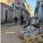 Nel centro dell'Avana semi-deserto un ragazzo guida un bici-taxi mentre un anziano si allontana. Una montagna di rifiuti giace sul ciglio della strada