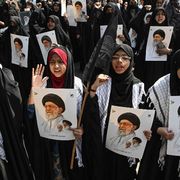 Una folla di donne con il lungo abito nero e la testa velata tengono in mano fotografie di Khamenei in segno di protesta