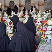 Donne velate di nero, di spalle davanti alle tombe ornate di nastri gialli e fiori con le fotografie di giovanissimi