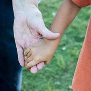 Due mani che si stringono: quella di un adulto e di un bimbo adottato