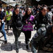 Una ragazza con un giubbino catarifrangente rosa, indossato dagli attivisti di "Standing Together", portata via da due poliziotte in mezzo a una manifestazione