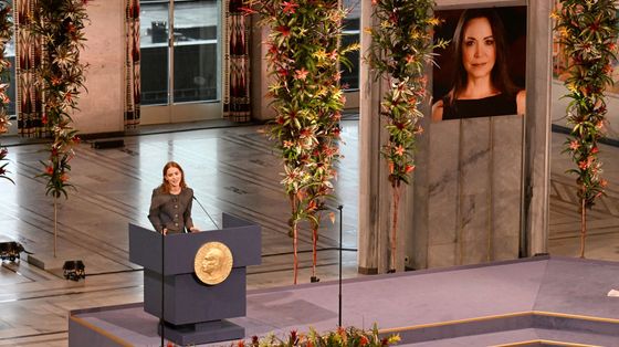 Sul palco del Premio Nobel per la Pace, agghindato di fiori, una giovane donna parla dal podio. Sullo sfondo, un grande ritratto dell'assente Machado