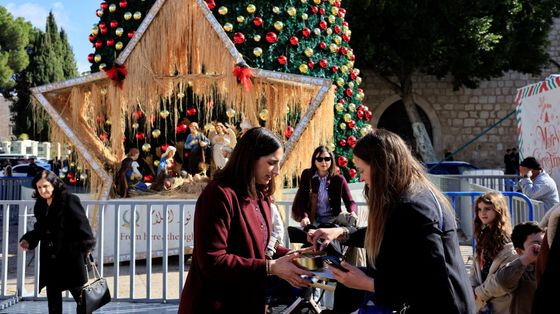 Donne fanno acquisti davanti a una gigantesca stella e a un albero di Natale, sullo sfondo il muro della Basilica della Natività