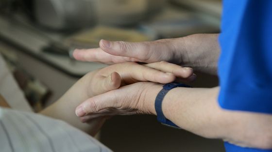 Un'infermiera stringe le mani di un malato di cancro in un reparto di cure palliative
