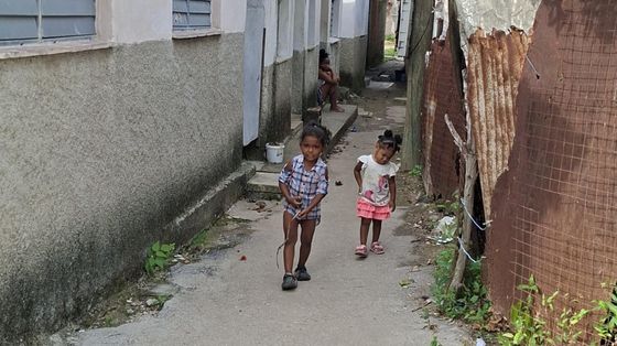 Due bambini cammino in un viottolo sterrato di una baraccopoli dell'Avana su cui si affacciano casupole di compensato e lamiera