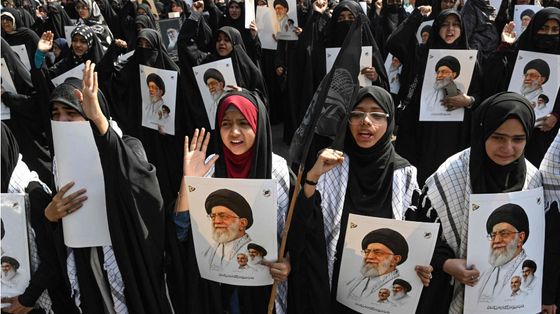 Una folla di donne con il lungo abito nero e la testa velata tengono in mano fotografie di Khamenei in segno di protesta