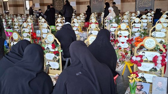 Donne velate di nero, di spalle davanti alle tombe ornate di nastri gialli e fiori con le fotografie di giovanissimi