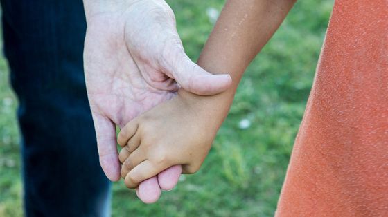 Due mani che si stringono: quella di un adulto e di un bimbo adottato