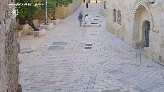 Una vasta via piastrellata, con pochissime persone: un uomo aggredisce alle spalle una suora in abito bianco e velo nero