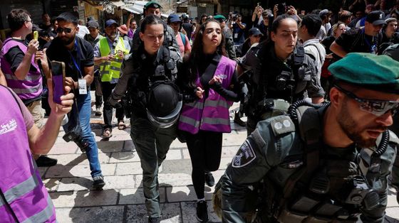 Una ragazza con un giubbino catarifrangente rosa, indossato dagli attivisti di "Standing Together", portata via da due poliziotte in mezzo a una manifestazione