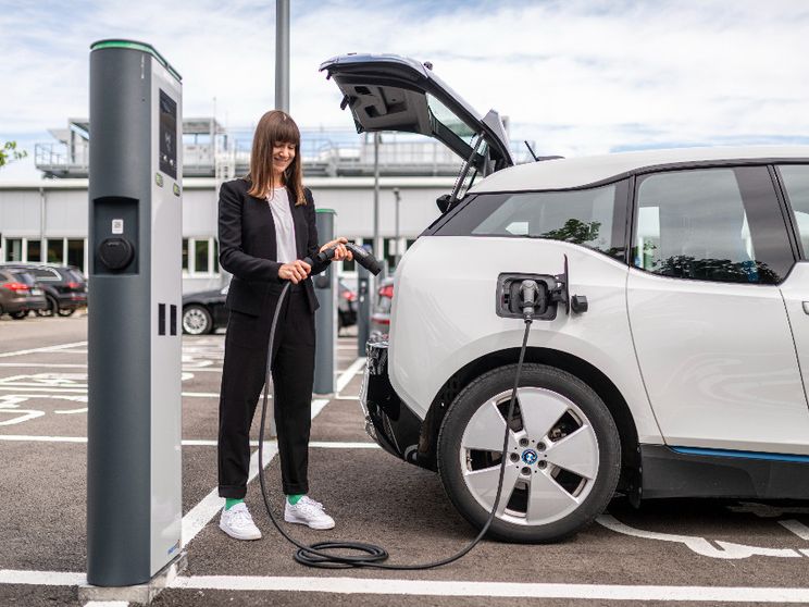 Una ragazza ricarica la propria auto elettrica da una colonnina pubblica