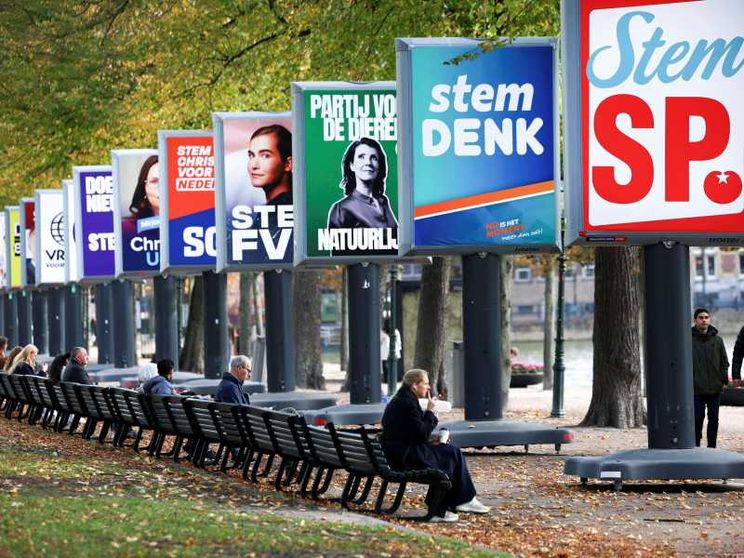 Una persona seduta su una panchina in un parco osserva dei grandi cartelloni elettorali con i simboli e gli slogan dei partiti