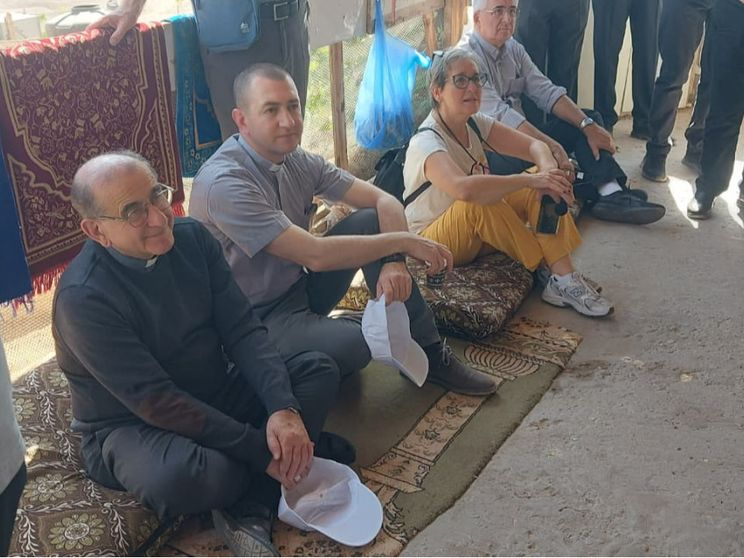 Nella fotto si vedono l’arcivescovo di Milano Mario Delpini seduto a terra in un villaggio beduino con altri partecipanti al recente pellegrinaggio in Terra Santa