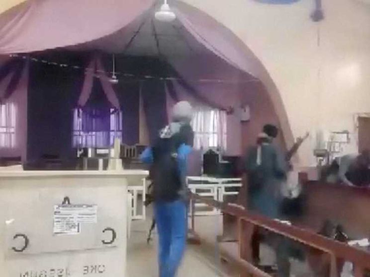In un fermo immagine da video, due uomini armati, in piedi di spalle, a fianco di un altare e tra le panche