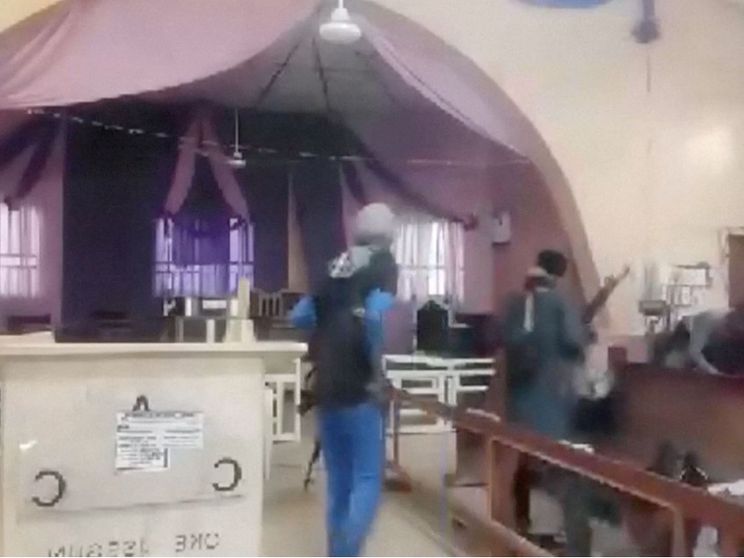 In un fermo immagine da video, due uomini armati, in piedi di spalle, a fianco di un altare e tra le panche