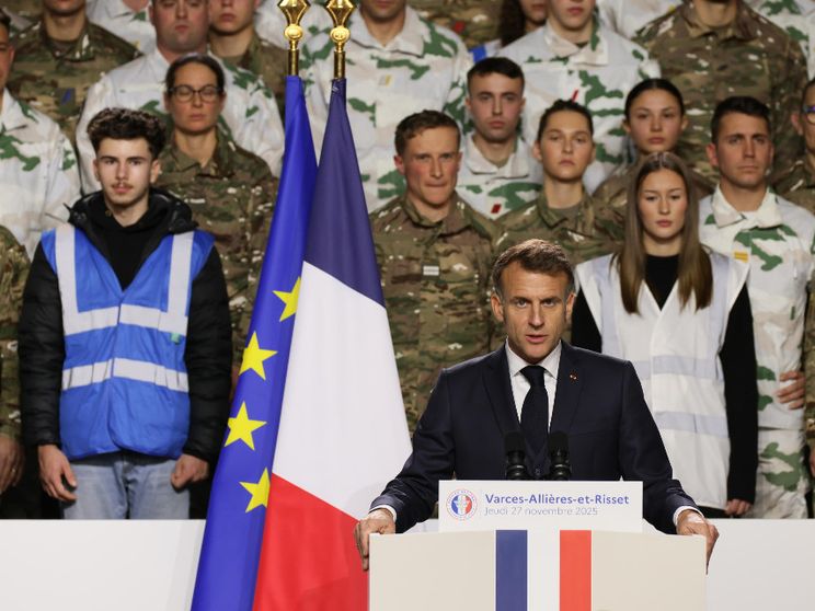 Il presidente francese Macron accanto alla bandiera francese e a quella dell'Unione Europea. Alle sue spalle uomini e donne in uniforme militare