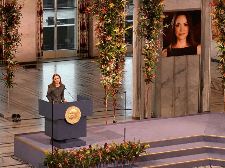 Sul palco del Premio Nobel per la Pace, agghindato di fiori, una giovane donna parla dal podio. Sullo sfondo, un grande ritratto dell'assente Machado