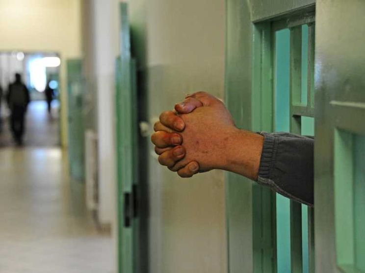 Due mani che sporgono dalle sbarre di un carcere