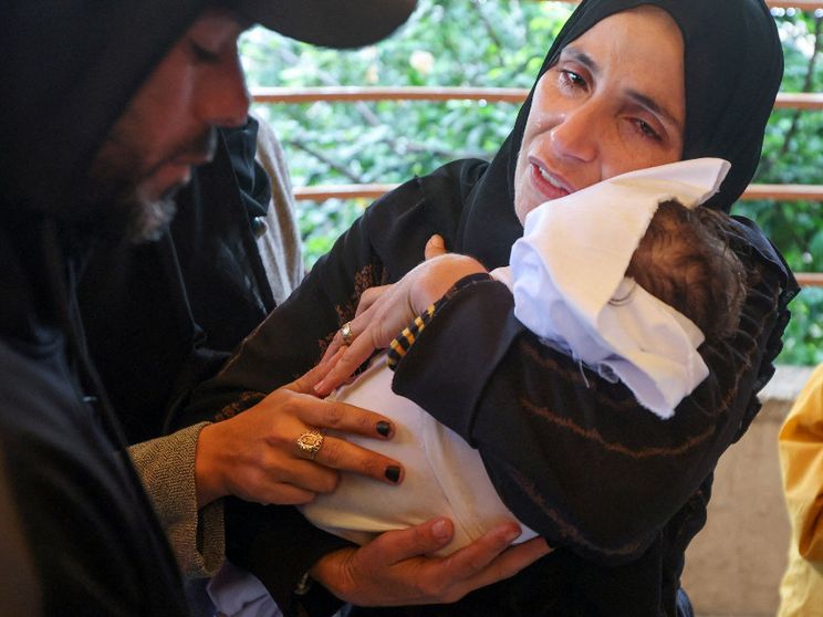 Una donna vestita di nero, con la testa velata e il volto rigato di lacrime, tiene fra le braccia un corpicino avvolto in un sudario bianco
