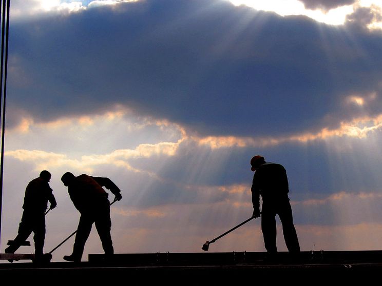 L'immagine mostra tre uomini che stanno lavorando su un ponteggio alla luce di un tramonto