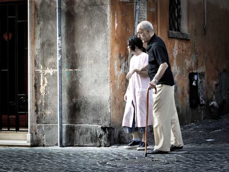 Una badante accompagna un anziano signore per le vie di Roma
