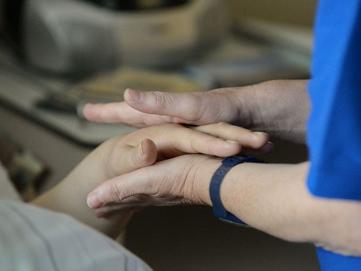 Un'infermiera stringe le mani di un malato di cancro in un reparto di cure palliative